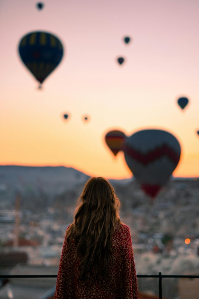 pexels-photo-3889726-3889726 A woman watches hot air balloons at sunrise in Cappadocia, Turkey, creating a breathtaking view.